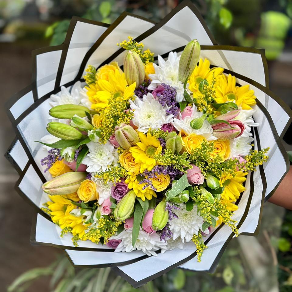 Yellow lilies and mixed flower bouquet wrapped in white paper — lilies vs roses gift guide.